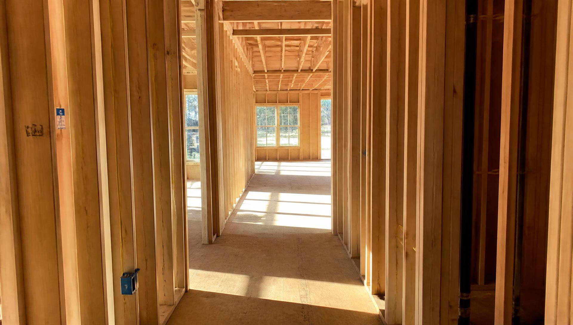 Walking through the framed interior of a new home toward a sunlit living space